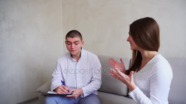 Smart doctor gives instructions and advice girl in medical office, sitting on sofa background of gray wall. — Stock Video