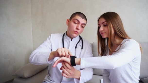 Portraits de médecin masculin intelligent, qui explique de fille à patient comment utiliser Smart Watch pour surveiller leur santé et s'asseoir sur le canapé dans le bureau des hôpitaux . — Video