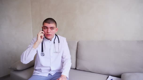 Dokter guy op mobiel geeft advies aan patiënten zittend op de Bank in het kantoor van ziekenhuis. — Stockvideo