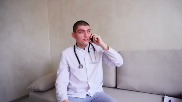 Portrait of doctor guy who on mobile gives advice to patients sitting on couch in office of hospital. — Stock Video