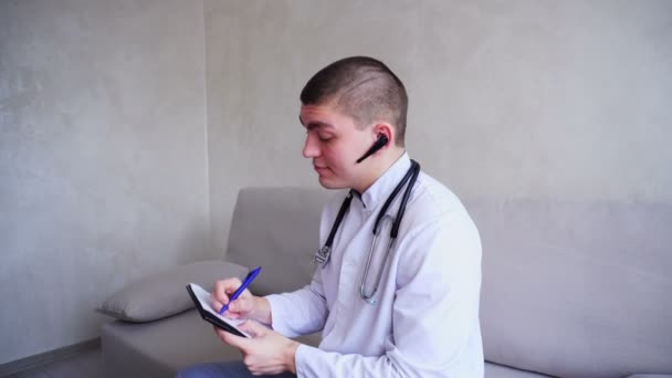 Moderní lékař hovoří o pacienta hesdphones a zapíše do recepce, sedí v kanceláři kliniky během dne. — Stock video