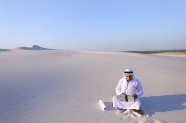 H üzerinde çölde kum üstünde laptop ile oturan Müslüman erkek mimar