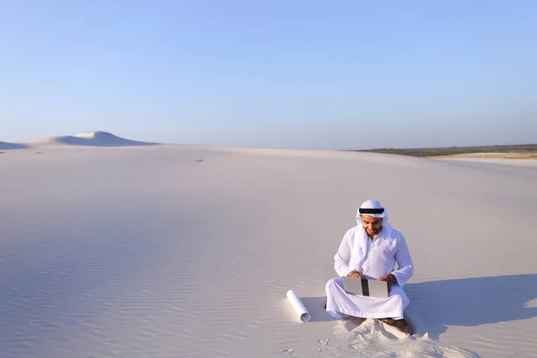 Muslimska manliga arkitekt som sitter med laptop på sand i öknen på h — Stockfoto