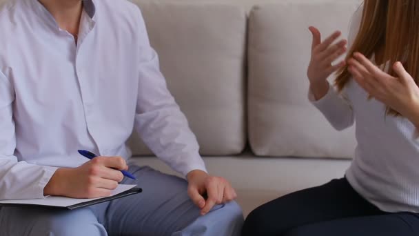 Frau kam zum Arzt, der zuhört und schreibt. Mann und Frau sitzen in Arztpraxis auf Couch vor grauem Hintergrund. — Stockvideo