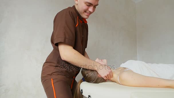 Guy masajista amasa cuello de chica joven, que se encuentra en el sofá en la sala de cosmetología brillante . — Vídeos de Stock