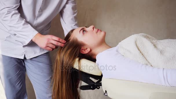 Красивый парень массажист делает массаж головы для девушки клиента, которая лежит на диване в офисе врача в течение дня . — стоковое видео