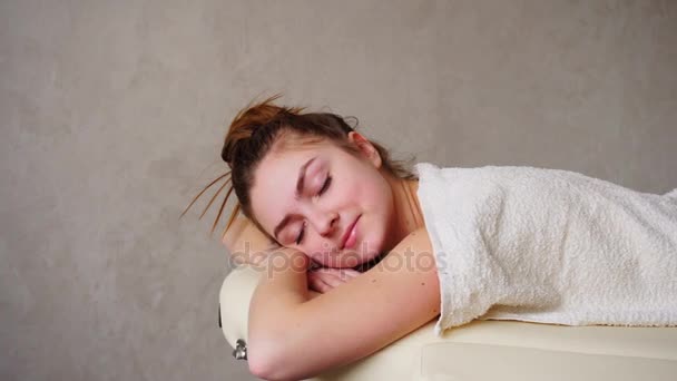 Piękna kobieta relaksuje po masażu i patrzy, leżąc na kanapie pod ręcznik w gabinecie lekarskim jasne. — Wideo stockowe
