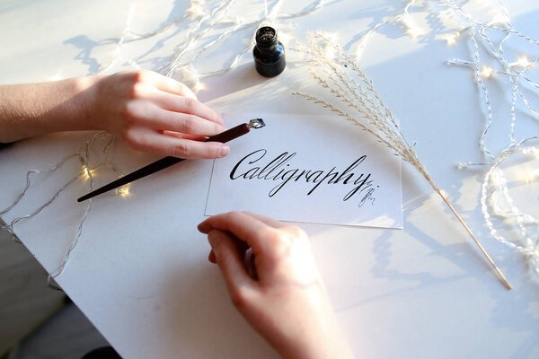 Girl writes pen fountain calligraphic letters, sitting at table