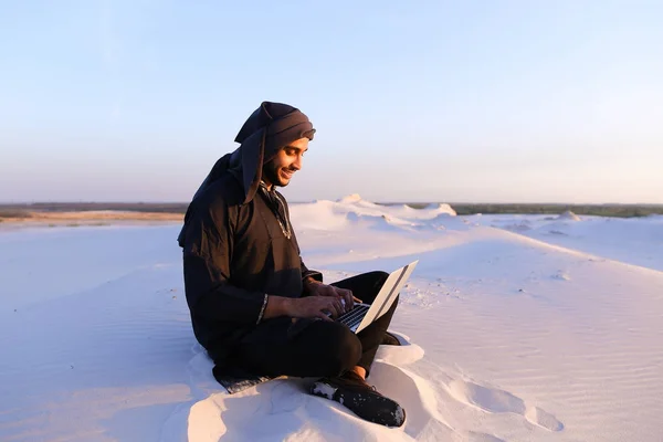 Vzdělaný Arab student využívá notebook a funguje, seděl na písku uprostřed — Stock fotografie
