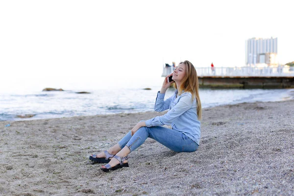 Όμορφη γυναίκα να μιλάει στο κινητό με χαμόγελο και να κάθεται σε παραλία n — Φωτογραφία Αρχείου