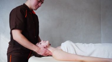 Güçlü elleriyle adam masör boyun parlak kozmetik odasında kanepede yatan genç kızın, kneads.