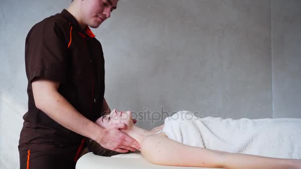 Guy masajista con las manos fuertes amasa el cuello de la joven, que se encuentra en el sofá en la sala de cosmetología brillante . — Vídeos de Stock