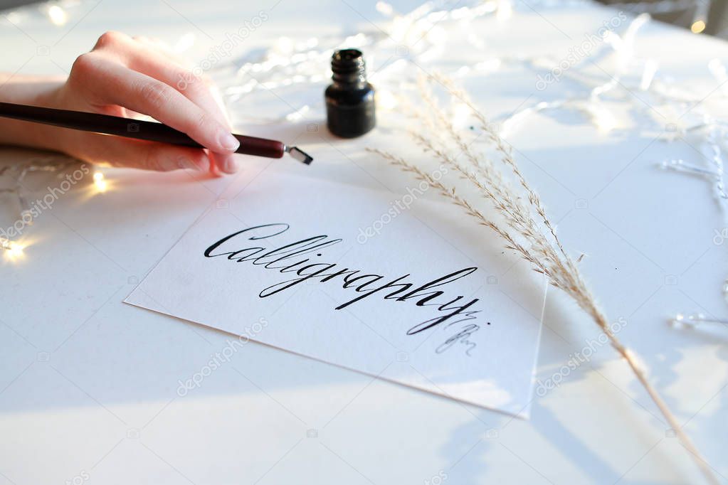 Female master of lettering of ink writes word on paper, sitting