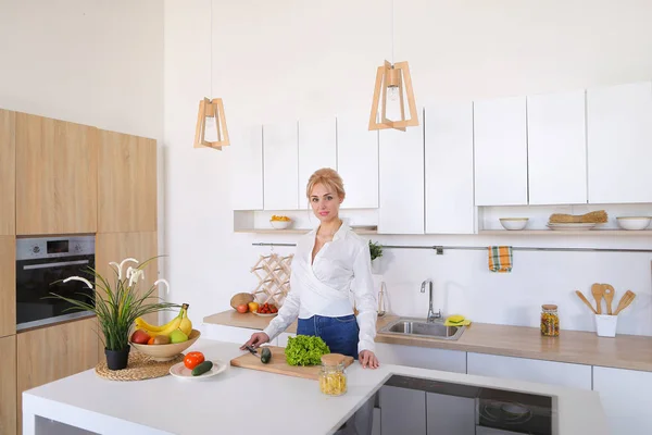 Attractive female housewife cuts cucumber with knife and smiles,