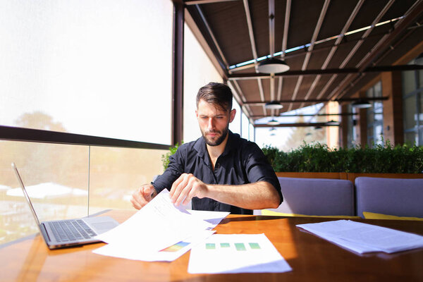 Office worker sorting papers on table near laptop.