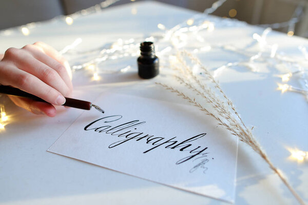 Female master of lettering of ink writes word on paper, sitting