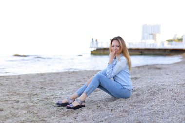 Gülümseyen genç kadın kumsalda aittir ve kamera, oturan pozlar