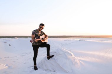 Arap yakışıklı arasında kum tepe üzerinde duran gitar çalmak