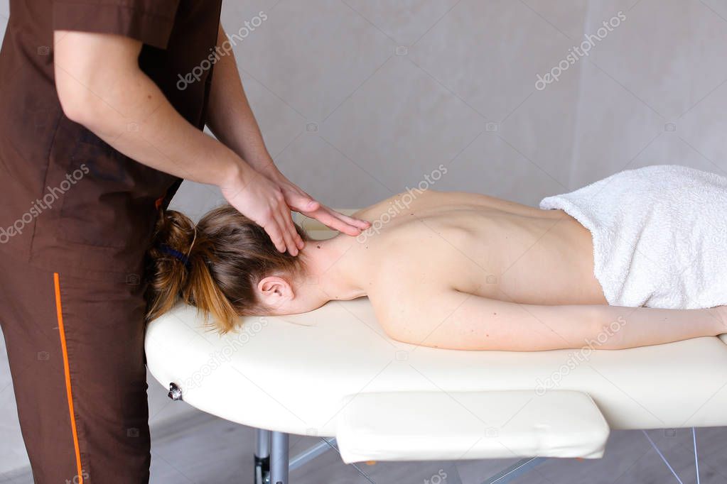 Male masseur with strong hands kneads neck of young woman who li