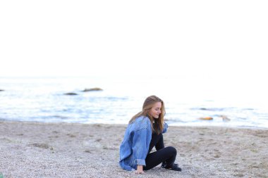 Gülümseyen genç kadın kumsalda aittir ve kamera, oturan pozlar