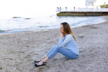 Gülümseyen genç kadın kumsalda aittir ve kamera, oturan pozlar