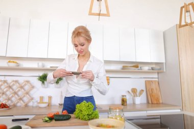 Mutfak kız smartphone elinde tutan ve sebze fotoğrafı çeker