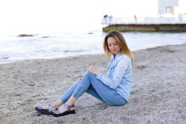 Gülümseyen genç kadın kumsalda aittir ve kamera, oturan pozlar