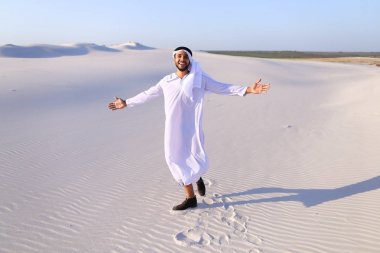 Happy Arab man walks in middle of white desert and enjoys life o clipart