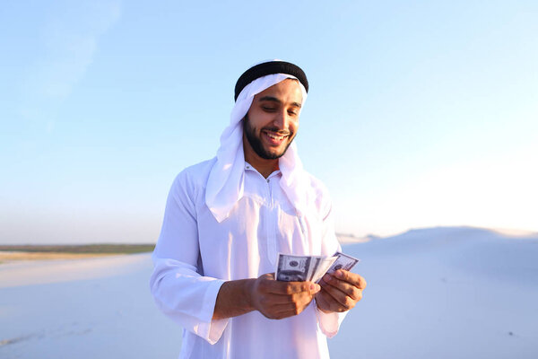 Successful Arab sheikh considers banknotes and happy, standing i