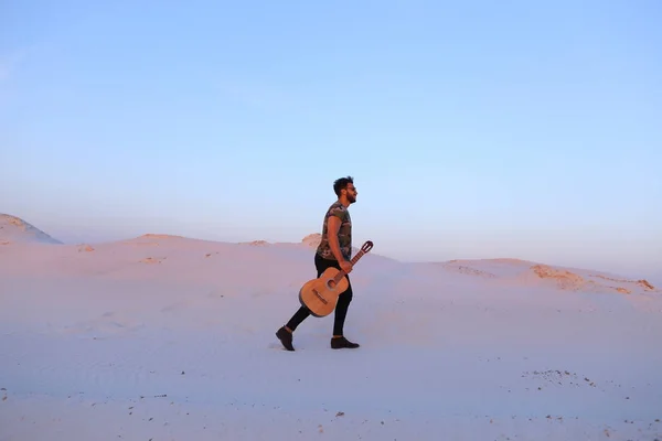 Stately Muslim young man walks with guitar in hands through dese