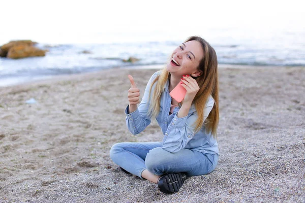 Adorável menina tagarelice no telefone com sorriso e senta-se na praia n — Fotografia de Stock