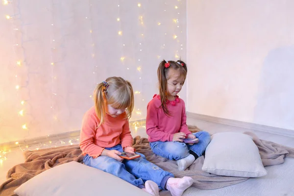 Happy little girls use smartphones for entertainment and sit on — Stock Photo, Image