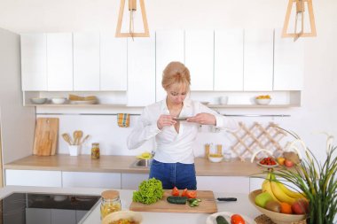 Mutfak kız smartphone elinde tutan ve sebze fotoğrafı çeker