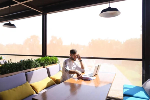 Процветающий менеджер по продажам читает документы, используя ноутбук за столом — стоковое фото