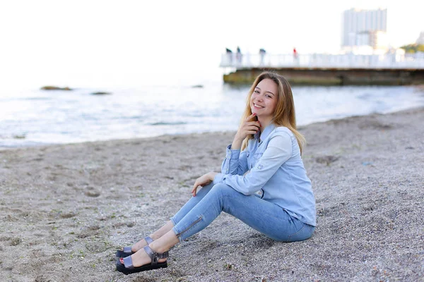 Χαμογελαστά νεαρή γυναίκα στηρίζεται στην παραλία και θέτει στην κάμερα, κάθεται — Φωτογραφία Αρχείου