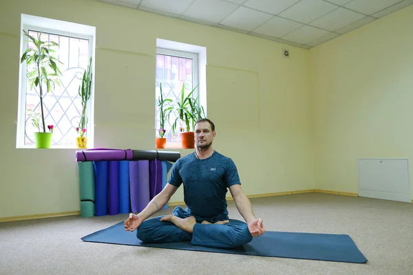 Knappe man zittend op de vloer op tapijt voor yoga in de lotuspositie — Stockfoto