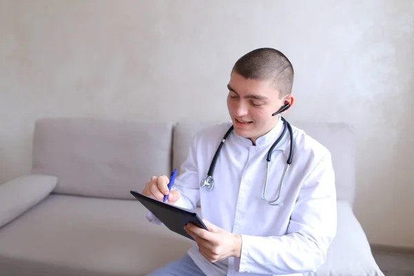 Modern male doctor talks to patient by bluetooth and writes to r