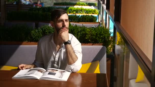 Handsome illustrator watching magazine pictures at table. — Stock Video
