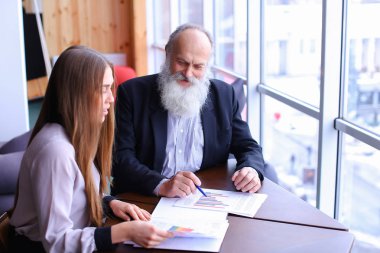 Yaşlı patron adam işaretleri belge raporları ile genç asistanı ile