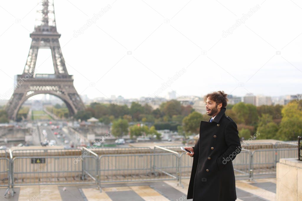 Mulatto laughing guy around Eiffel Tower with smartphone