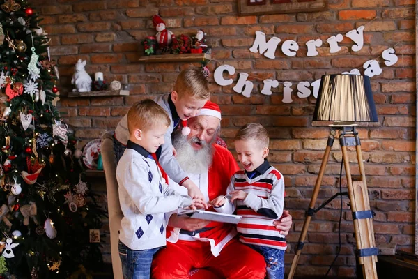 Caras energéticos jogar em tablet junto com Santa em roo festivo — Fotografia de Stock