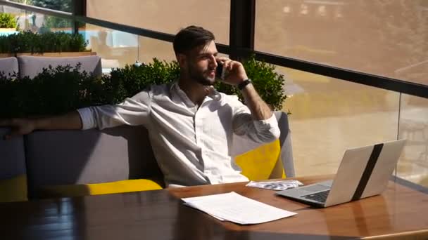 Fastighetsmäklare pratar av smartphone och arbetar med laptop vid bord. — Stockvideo