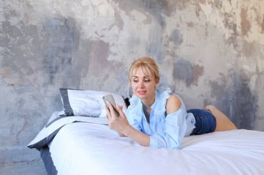 Sevimli kadın elinde tutan ve akıllı telefon kullanan, büyük üzerinde yatıyor