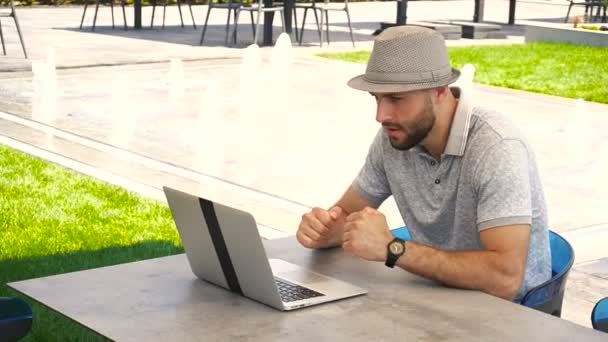 Bonito macho divertido assistindo jogo de futebol com laptop perto da fonte . — Vídeo de Stock