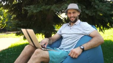 Dizüstü bilgisayar ve cam ile bakarak çanta sandalyede oturan zengin adam yüzünü kapatmak.