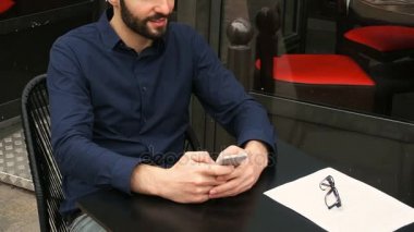 Kafeterya masada oturan ve yavaş hareket yüzüne yakından ile akıllı telefon tarafından sohbet mutlu adam.