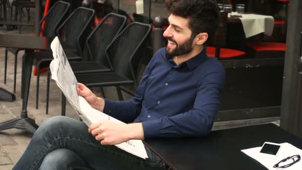 Un homme joyeux lisant un journal au café avec des lunettes et un smartphone sur la table au ralenti . — Video
