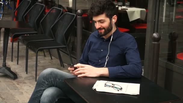 Estudiante escuchando música con smartphone y auriculares en la mesa de la cafetería . — Vídeo de stock
