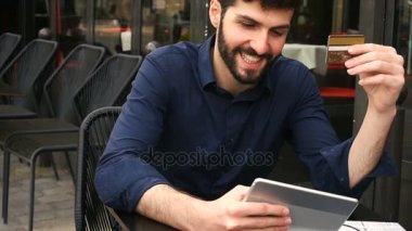 Mutlu adam alışveriş kartı ve yavaş hareket yüzüne yakından ile sokak kafede tablet ile online.