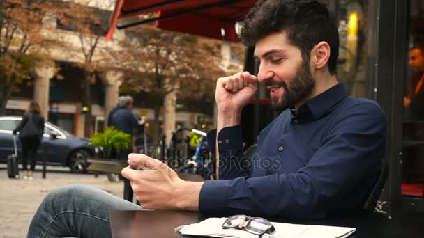 Процвітаючий менеджер з продажу радіє і спілкується зі смартфоном у вуличному кафе . — стокове відео